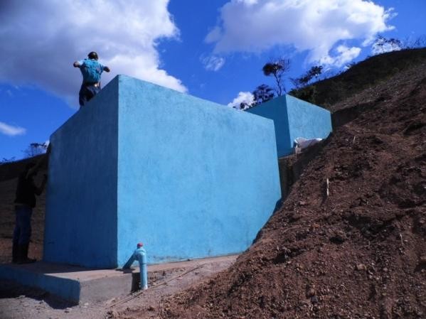 Blaues rechteckiges Gebäude (Wasserspeicher) neben einem Erdhügel und unter blauem Himmel