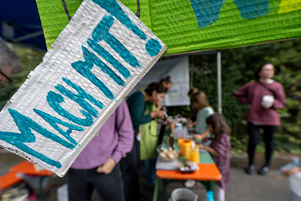 Ein Schild mit der blauen Aufschrift: Mach mit!; im Hintergrund ein Waffelstand.