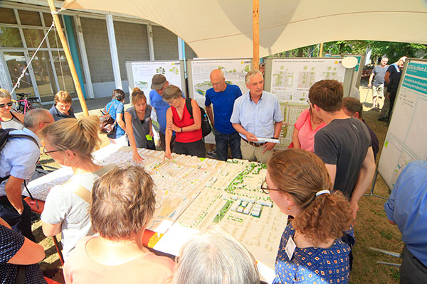Stadtteilkonzepte mit Bürgerbeteiligung - Beispiel, Foto: Schmidt-zero Tisch mit Plänen und Menschen stehen interessiert und diskutierend um den Tisch herum