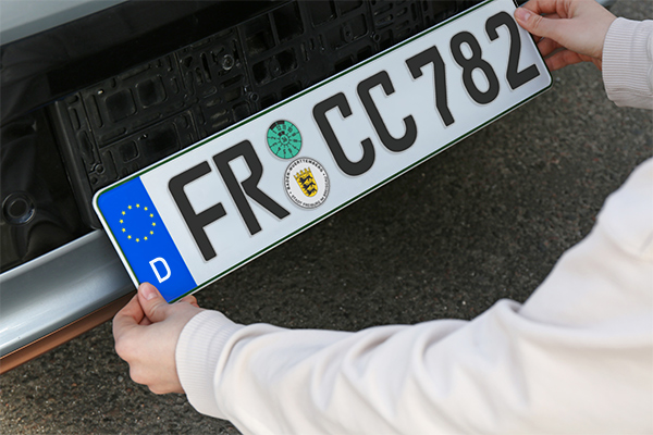 (Foto: Liudmila Chernetska/ istockphoto.com) Frau installiert das Fahrzeugkennzeichen draußen, Nahaufnahme