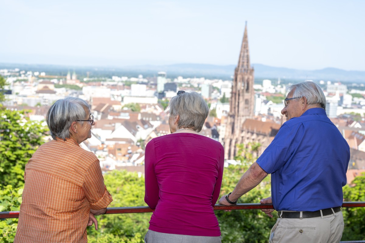 (Foto: Seeger / Stadt Freiburg) Drei ältere Personen blicken auf Freiburg mit dem Münster.