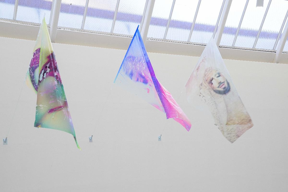 Foto: Marc Doradzillo Ausstellungsansicht von "Fields of Un/Rest". drei bunte wehende Fahnen, die an Glasstangen montiert sind