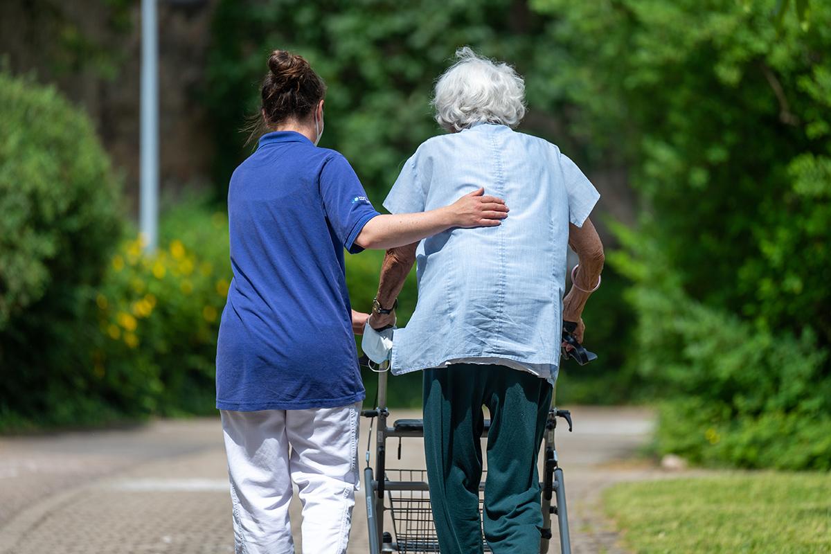 Eine Pflegerin hilft einer älteren Frau beim Gehen am Rollator