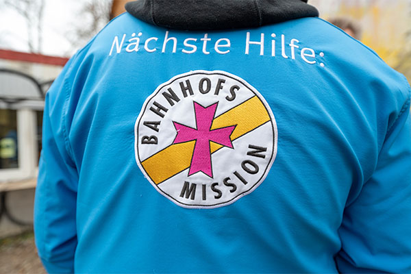 Blaue Jacke mit Aufdruck "Nächste Hilfe: Bahnhofsmission"