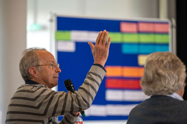 Ein Mann mit Mikrofon bei einer Infoveranstaltung streckt die Hand