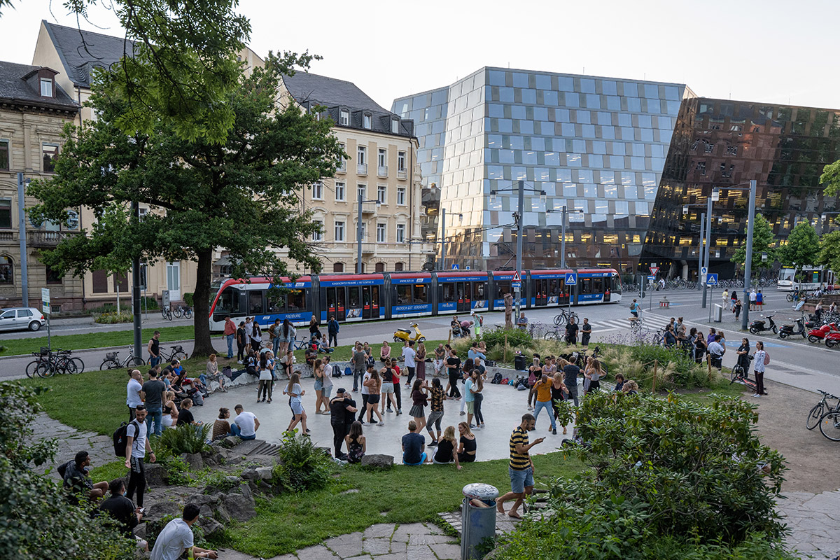 Tanzende Menschen im Tanzbrunnen, im Hintergrund die Unibibliothek Freiburg