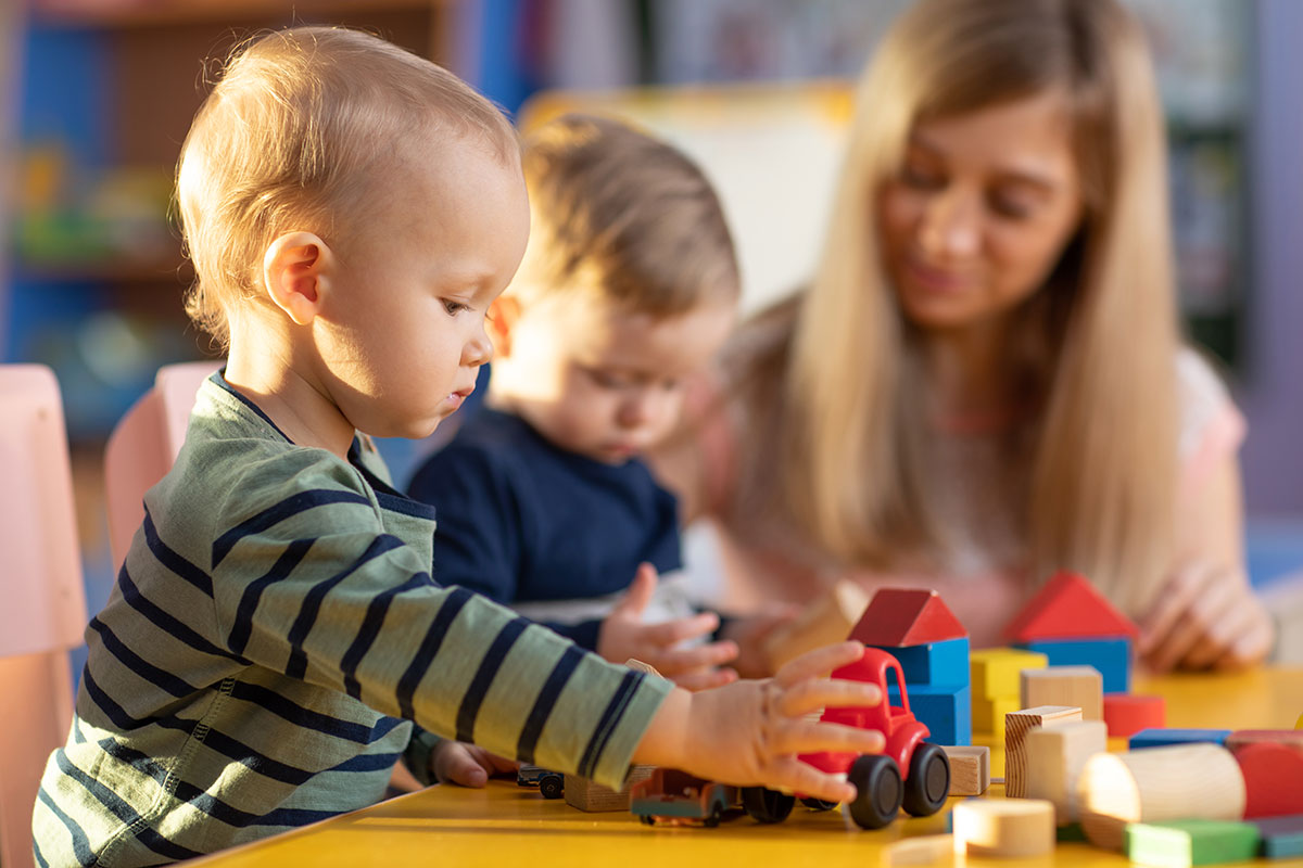 2 kleine Kinder spielen mit Bauklötzen, Erzieherin sitzt daneben