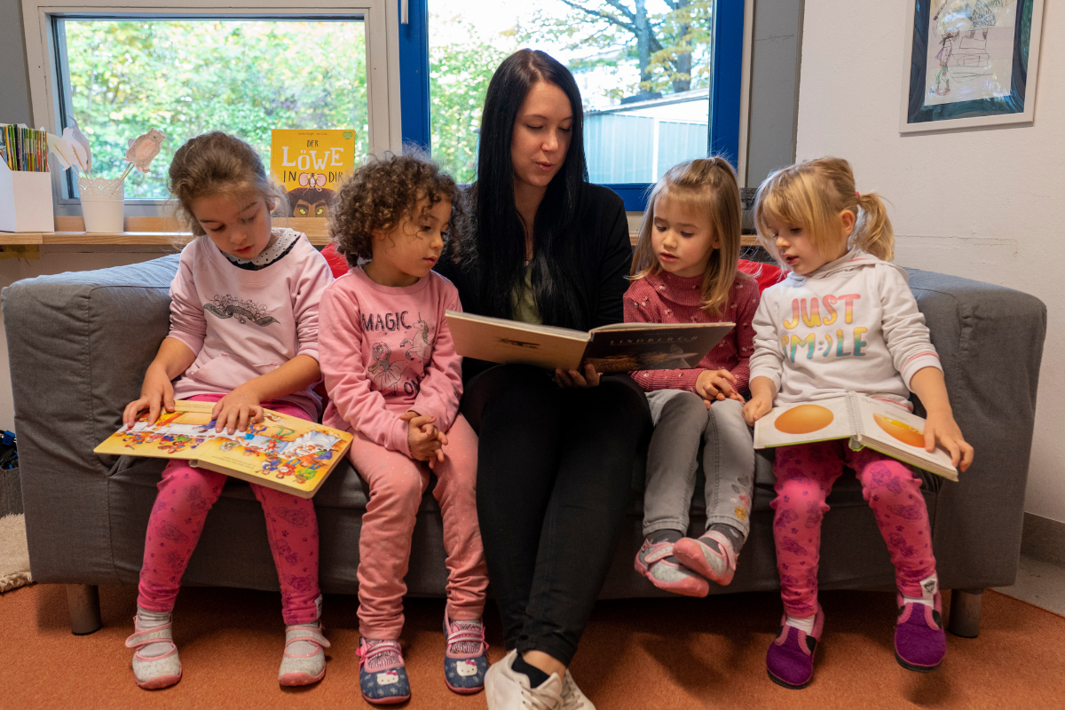 Eine Fachkraft betrachtet mit vier Kindern Bilderbücher.