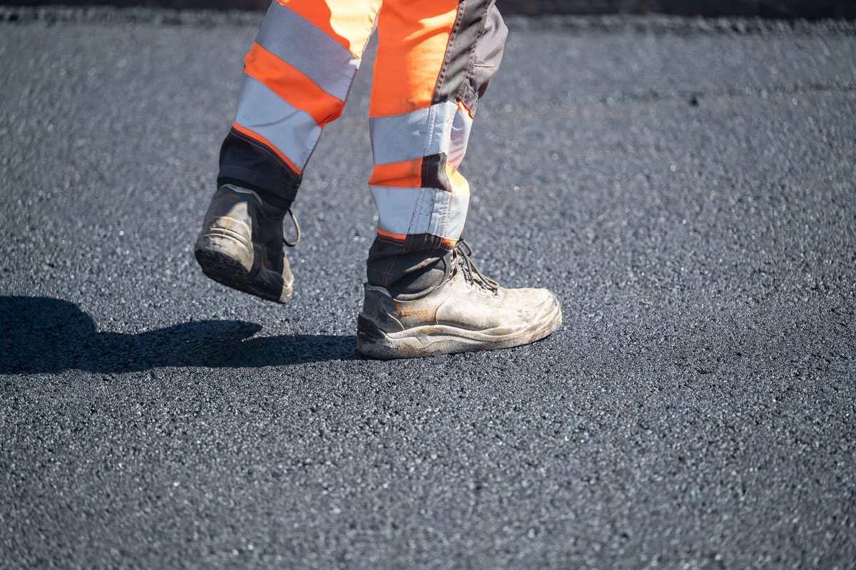 Straßenbauarbeiter*in läuft über frisch geteerte Straße
