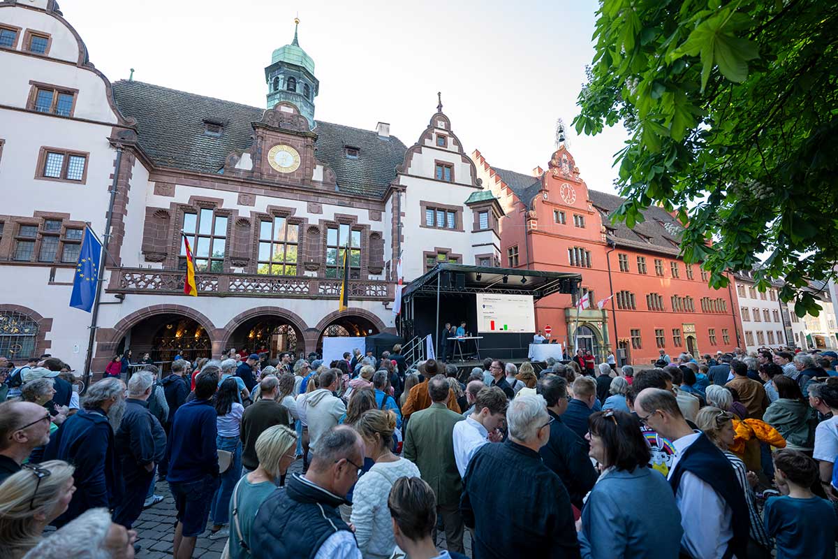 Läufer*innen beim Freiburg-Marathon rennen durch eine Straße. Am Seitenrand stehen Autos und Fans