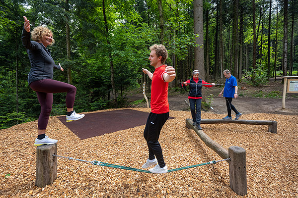 mehre Menschen an Klimmzugstangen im Wald