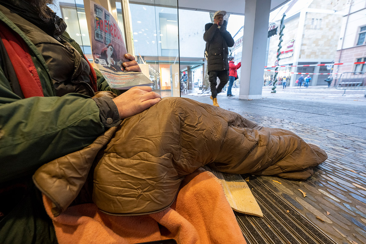 Obdachlose Person mit Schlafsack und Obdachlosenzeitung