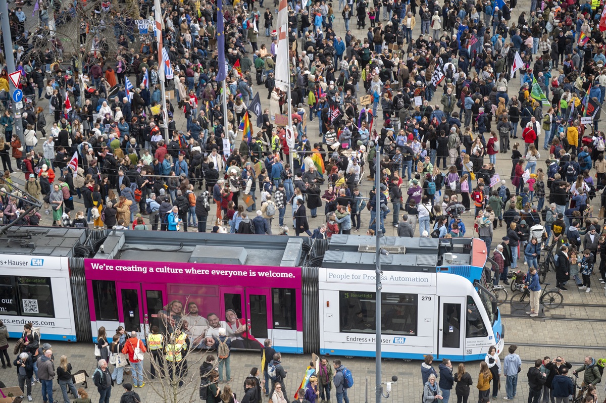 Eine Versammlung steht auf einem Platz und behindert die Straßenbahn.