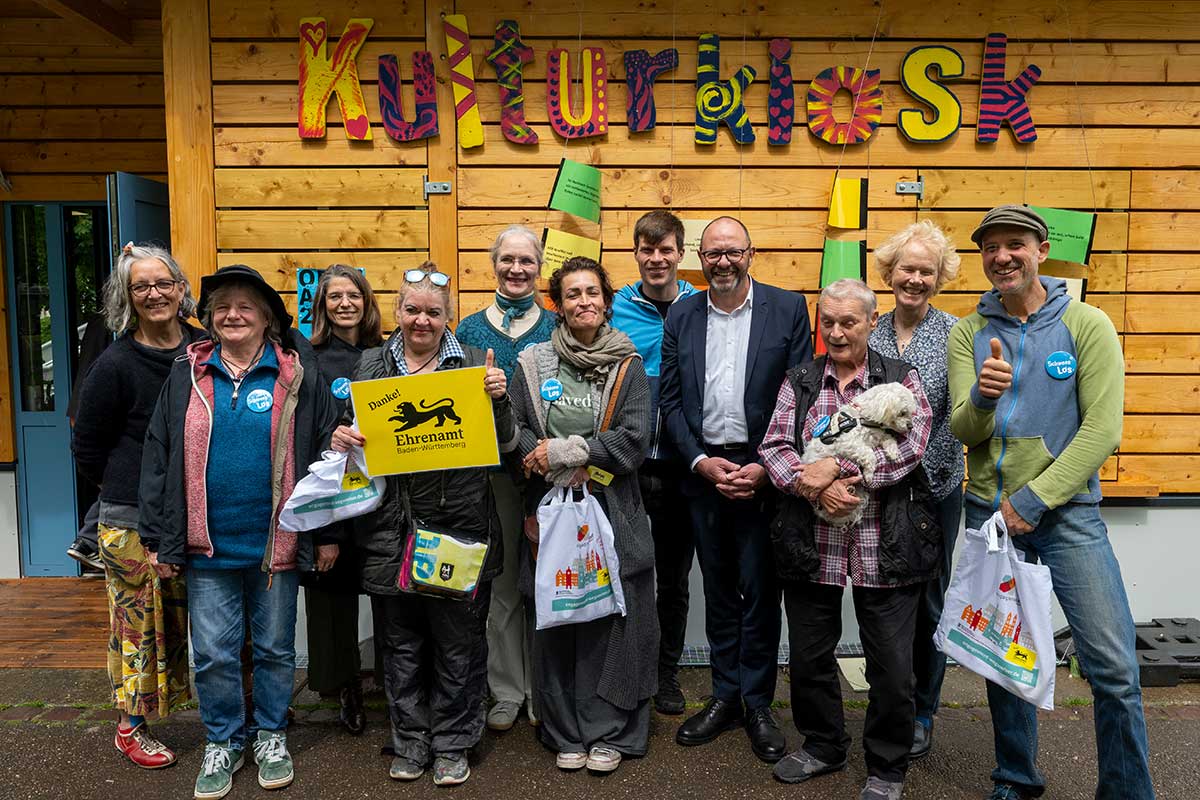 11 Menschen und ein Hund vor dem Kulturkiosk, eine hält ein Schild mit "Danke! Ehrenamt Baden-Württemberg"
