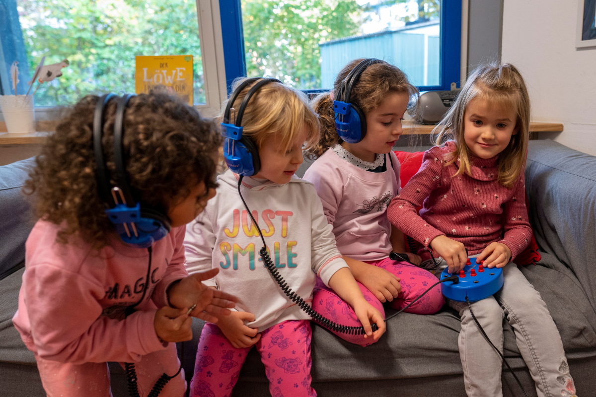 Vier Kinder sitzen auf einer Couch und tragen Kopfhörer.