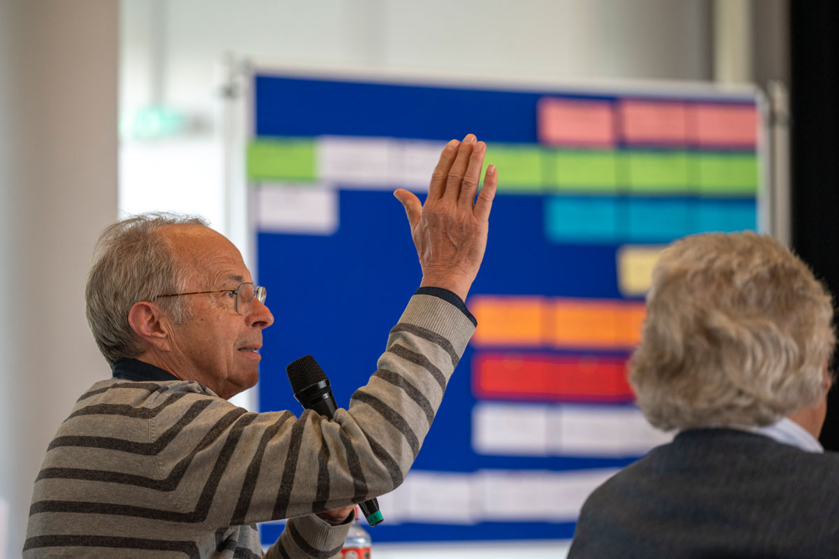 Ein Mann mit Mikrofon bei einer Infoveranstaltung streckt die Hand