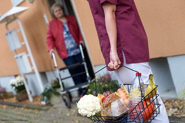 Grauhaarige Frau mit Rollator und eine Frau mit gefülltem Einkaufskorb