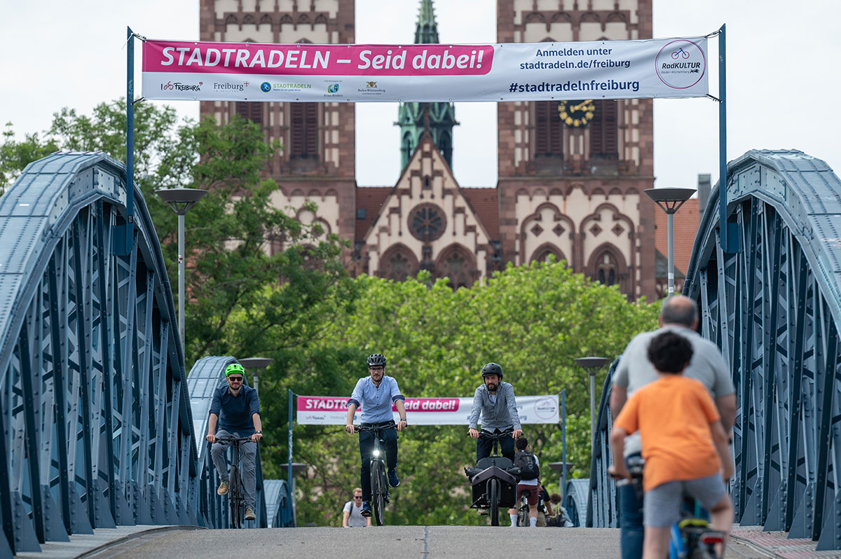 Banner fürs Stadtradeln über der Wiwili-Brücke, davor Radler_innen von hinten 