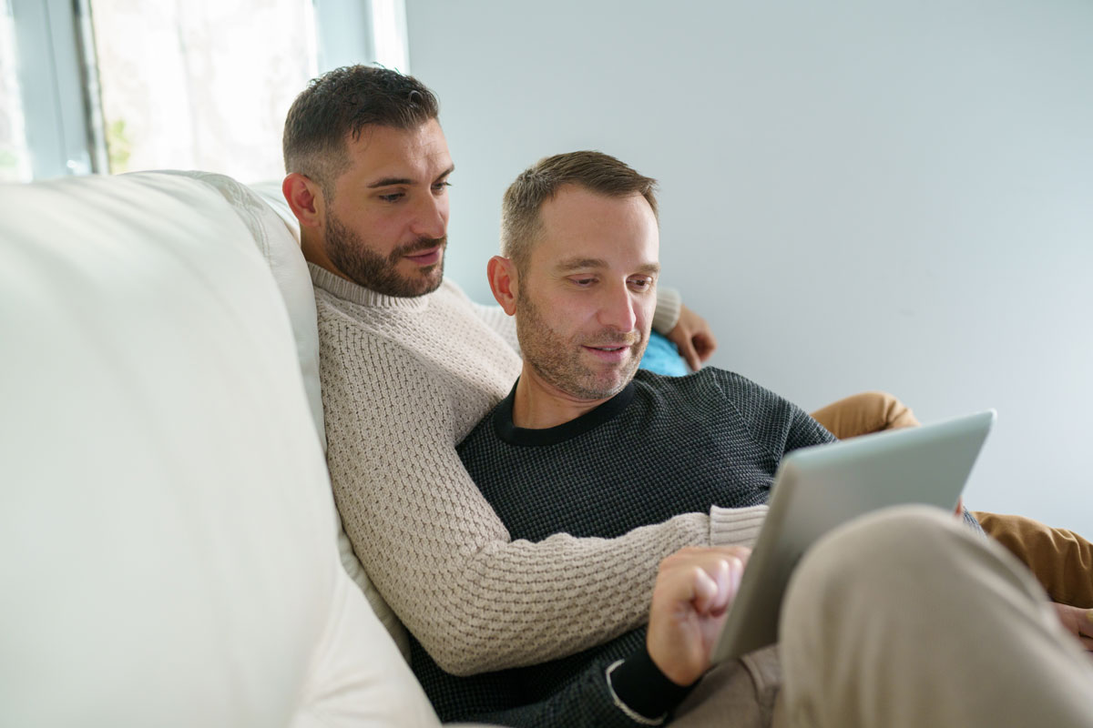 Zwei Männer auf einem Sofa schauen in ein Tablet