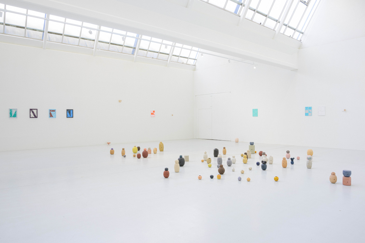 Foto: Marc Doradzillo Ausstellungsansicht von "Following – some kind of same – π". Auf dem hellen Galerieboden sind zahlreiche kleine keramische Skulpturen in organischen Formen und gedeckten Farben (Ocker, Grau, Rosa, Gelb) frei verteilt. An den weißen Wänden hängen kleinformatige Gemälde mit grafischen Motiven.