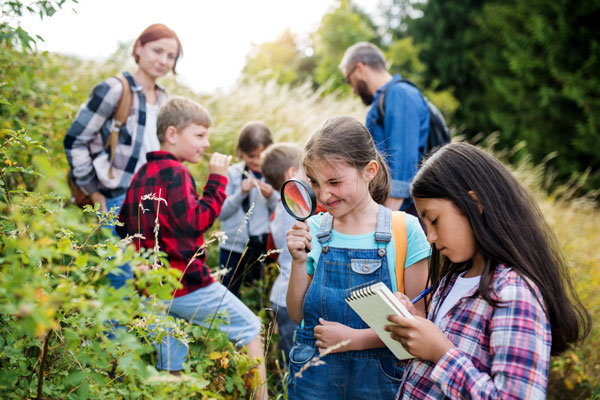 Eine Gruppe Kinder mit Lupe und Notizblock in der Natur