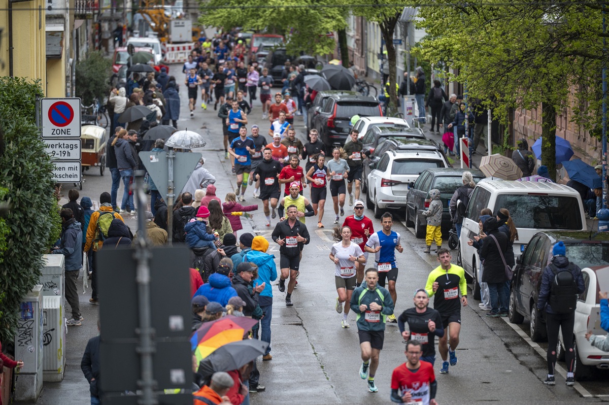 Läufer*innen beim Freiburg-Marathon rennen durch eine Straße. Am Seitenrand stehen Autos und Fans