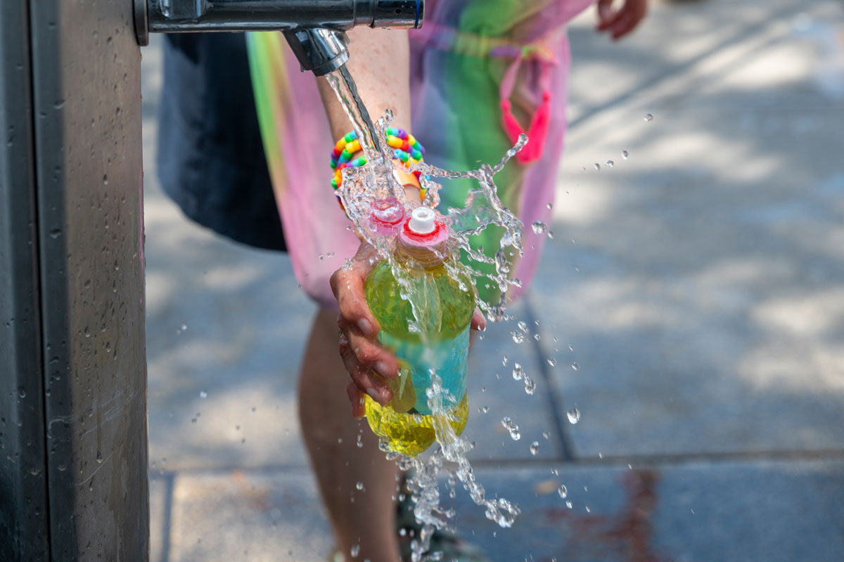 Jemand füllt unter einem Trinkbrunnen eine Flasche Wasser auf
