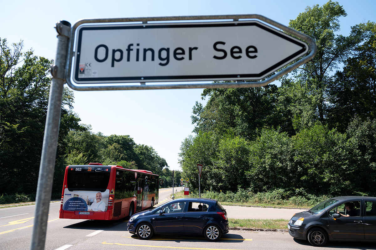 Schild "Opfinger See", dahinter ein Bus und zwei Autos