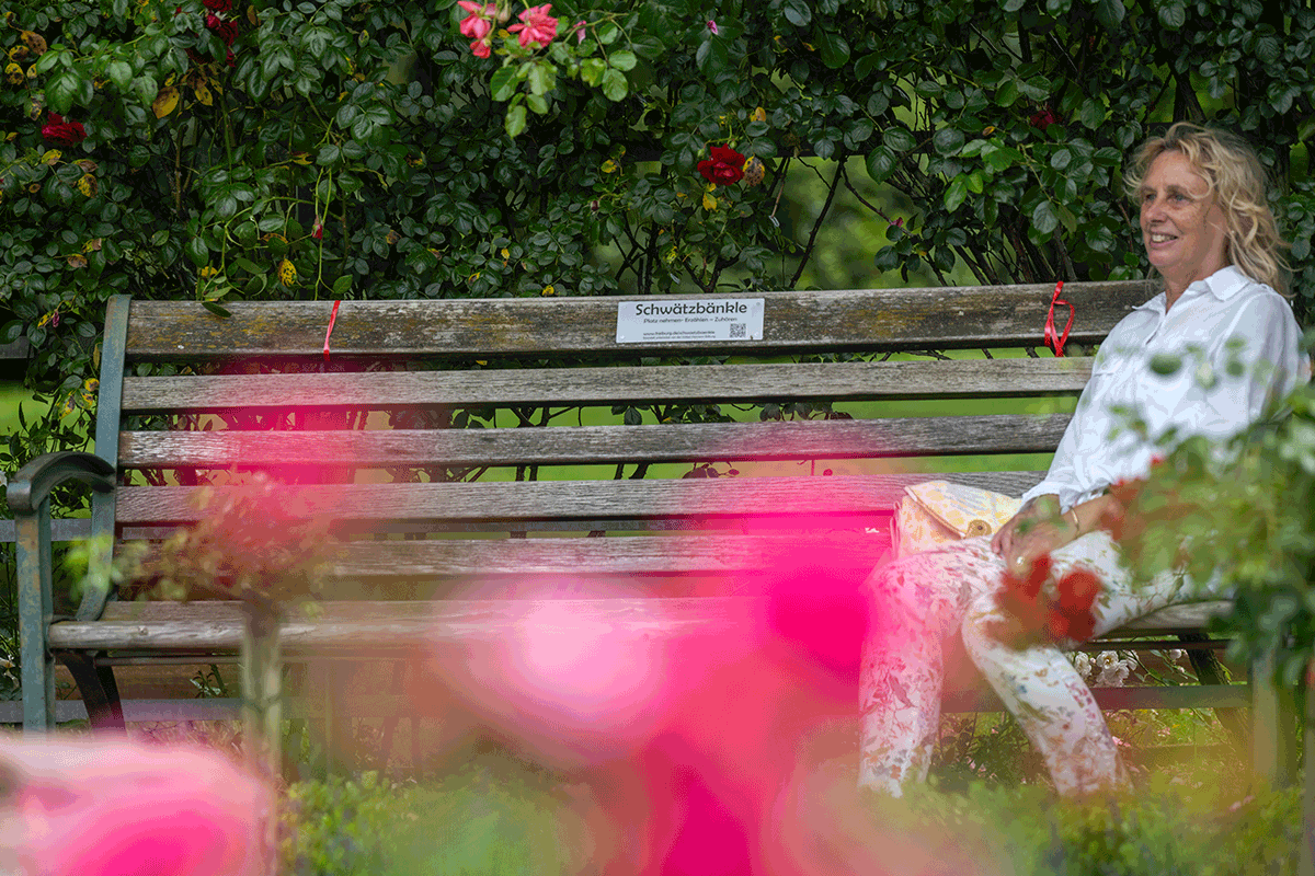 Frau auf einer Parkbank mit Schild "Schwätzbänkle"