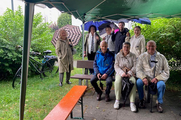 Ältere Menschen mit Regenschirmen vor und hinter dem Schwätzbänkle in Betzenhausen